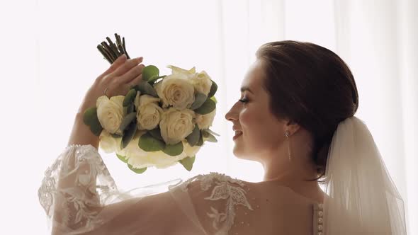 Bride in White Dress Staying Near Window with Flowers Bouquet Wedding Morning Preparations at Home