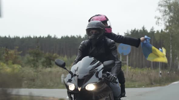 Confident Happy Couple of Young Bikers with Ukrainian Flag Driving Motorcycle Along the Road