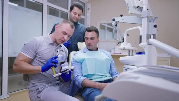 Serious Professional Caucasian Dentist Talking Showing Teeth Cast to Patient with Middle Eastern MD