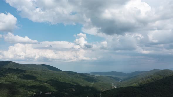 Aerial hyperlapse of fast moving clouds over forest green hills