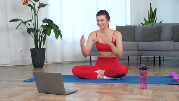 Sportive Smiling Woman in Sportswear Sitting on Yoga Mat at Home in Living Room