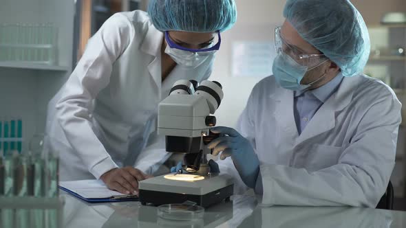 Medical Researchers Looking Through Microscope in Turns and Taking Notes, Lab