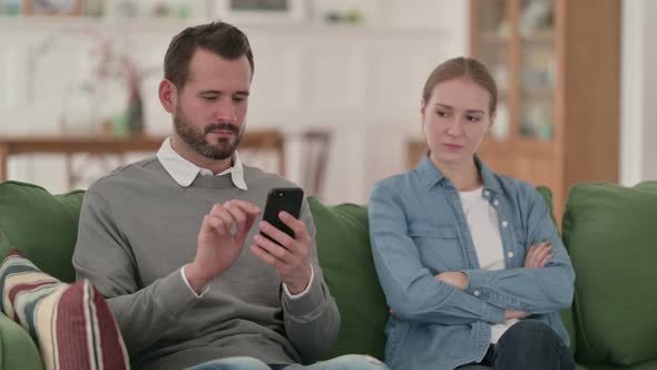 Middle Aged Man Busy with Smartphone Sitting Next To Angry Wife Woman