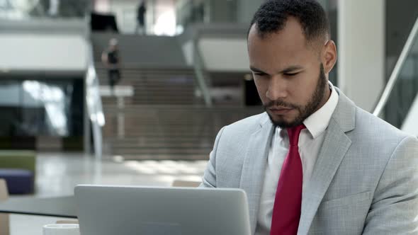 Focused Young Man Wearing Suit Working with Laptop at Cafe.