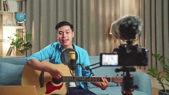 Asian Man Playing Guitar And Sing A Song. The Male Is Streaming For His Social Media Channel