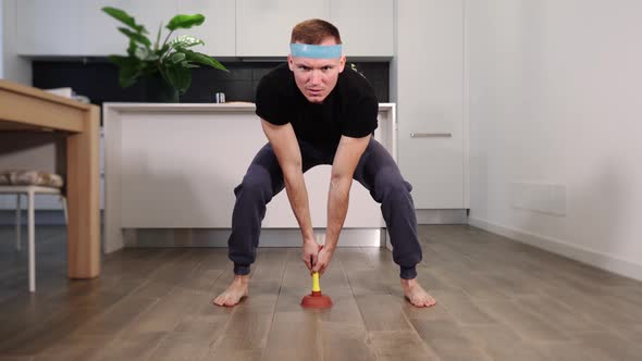 Sporty Guy Holds Plunger Pumping Brown Wooden Floor at Home