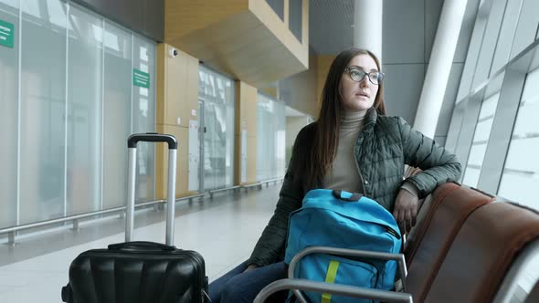 Young Tired Woman in Glasses is Waiting Her Flight in Airport Sitting in Hall