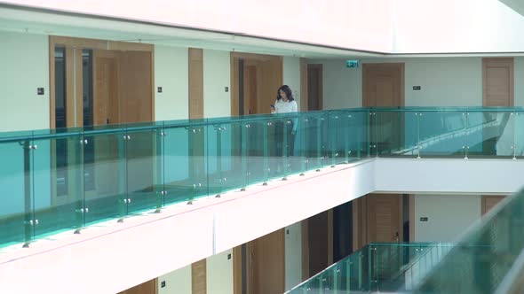 Business woman holding phone while walking down corridor.