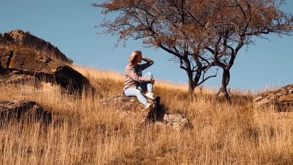 Girl Sits in Autumn on a Stone Near a Tree