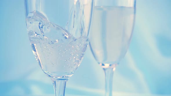 Sparkling wine is poured into a glass on a blue background. Slow motion.