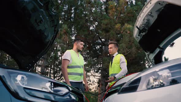 Two Men in a Green Safety Vest are Talking to Each Other Recharging Battery on the Road