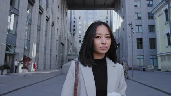 Pivoting Around Young Adult Asian Businesswoman Walking From Office with a Coffee Cup in Slow Motion