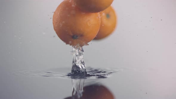 One fresh orange falls down onto a surface covered with freshwater and bounces in slow motion