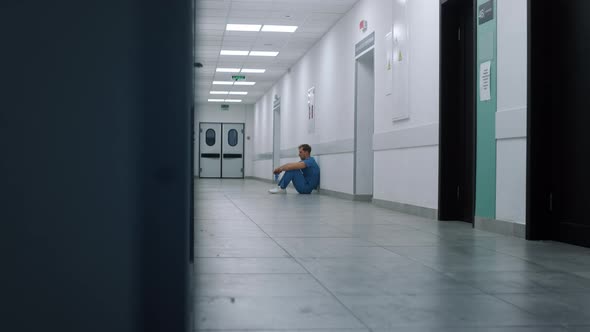 Stressed Doctor Sitting Leaning on Wall Hallway