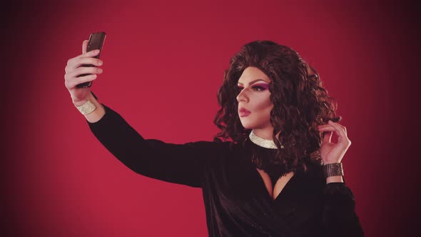 A Young Man Drag Artist in Extravagant Dress on the Red Background  Taking a Selfie and Smiling