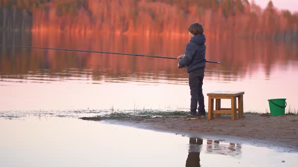 Little Boy is Fishing at Sunrise on the Lake