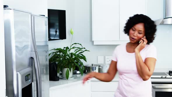 Woman talking on mobile phone while working in kitchen