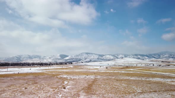 Flying over snowy fields towards the foothills of the Colorado Rockies during the day, aerial