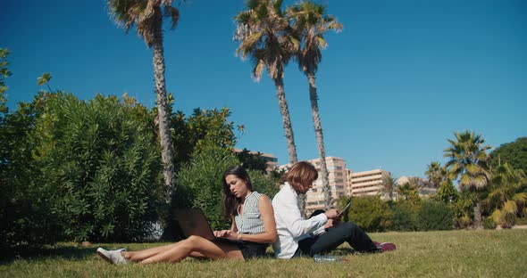 Freelance Couple Working Outdoor in Public Park Using Laptop Computer and Tablet