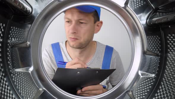 Washing machine repairman looks at drum and writes down list of works.