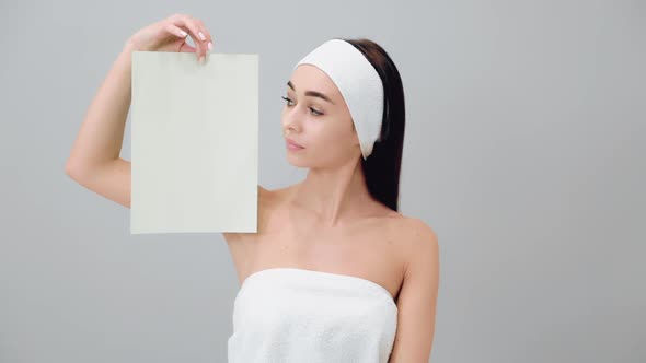 A young beautiful woman in a headband and a bath towel shows a white sheet.