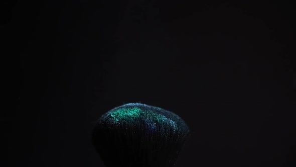 slow motion of a make up brush with blue powder explosion and burst on black background