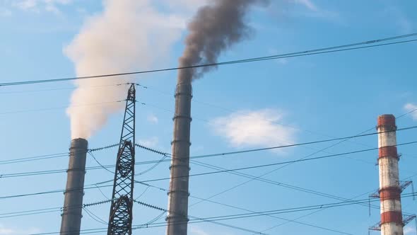 High Voltage Electric Pylons Against Coal Power Plant High Pipes with Black Smoke Moving Upwards