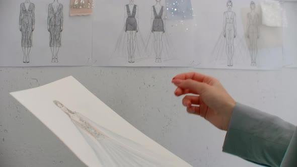 Female Fashion Designer is Choosing and Hanging Clothing Sketches to Wall for Her Newest Collection