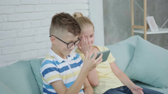 Close Up of an Excited Twins Kids Using Smartphone Sitting Together on Sofa