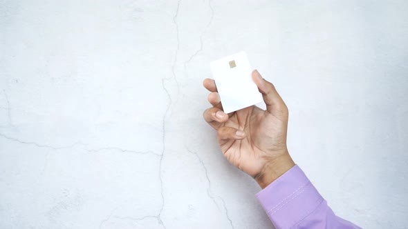 Person Hand Holding Credit Card Against a White Wall