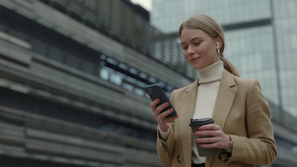 Woman in Earphones Walking on Street and Using Mobile