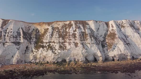 Drone flies low away from the White Cliffs of Dover, revealing beautiful turquoise sea in the foregr