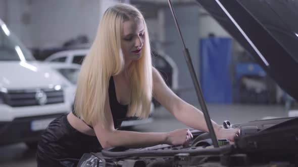 Close-up of Blond Caucasian Woman Tightening Screws in Open Car Hood. Beautiful Female Auto Mechanic