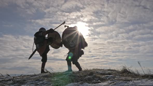 Two Warriors Viking Are Fighting with Axes and Shields on the Winter Meadow