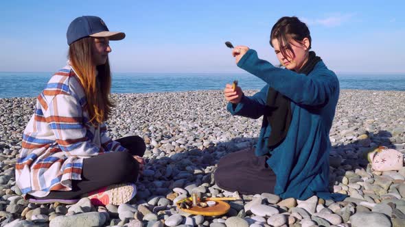 Two women are sitting on the seashore and preparing for a rape ceremony.