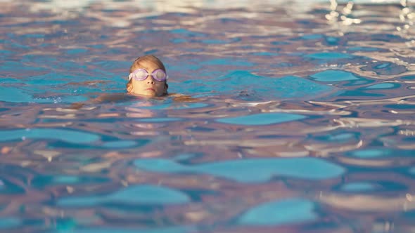 A Girl in a Bright Swimsuit with Swimming Goggles Dives Into a Pool with Clear Transparent Water