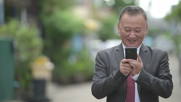 Mature Japanese Businessman Using Phone in the Streets Outdoors