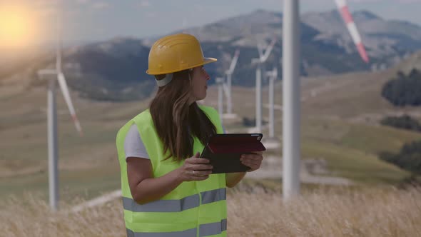 Woman engineer  in yellow hard hat and green uniform checking the wind turbine system