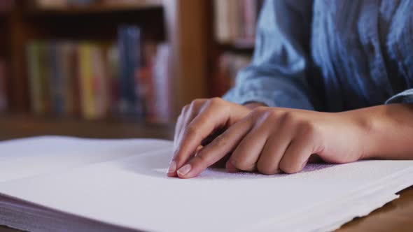 Asian female student sitting and touching a page of a braille book at library