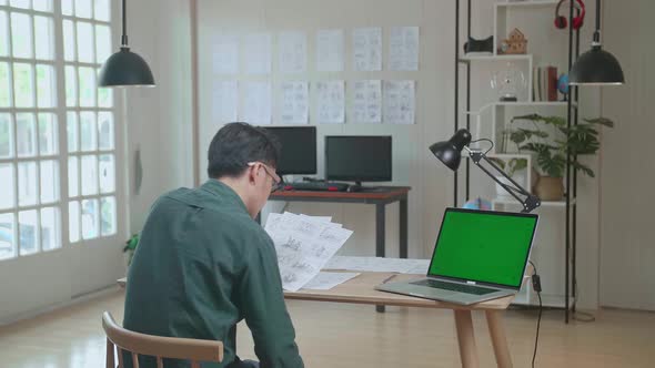Creative Designer Works On A Storyboard, Looks At His Sketches With Green Screen Laptop Computer