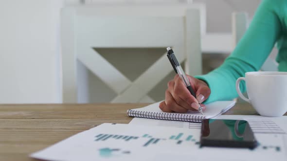 Mid section of african american woman taking notes while working from home