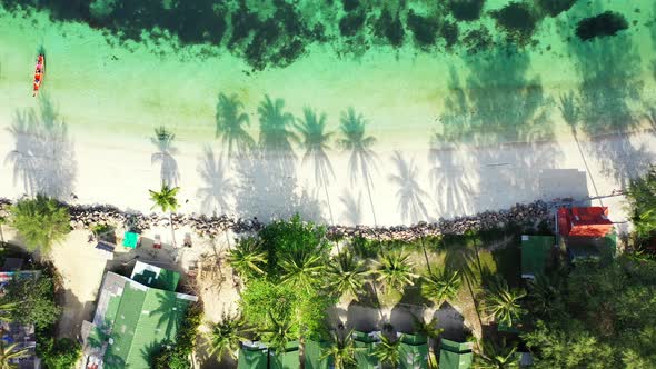 Peaceful exotic beach with palm trees shade over white sand washed by calm water of turquoise lagoon