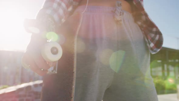 Midsection of caucasian woman holding skateboard on sunny day