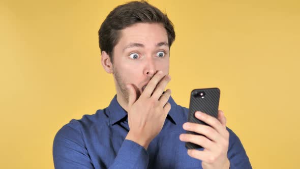 Wow Surprised Casual Young Man Using Smartphone on Yellow Background
