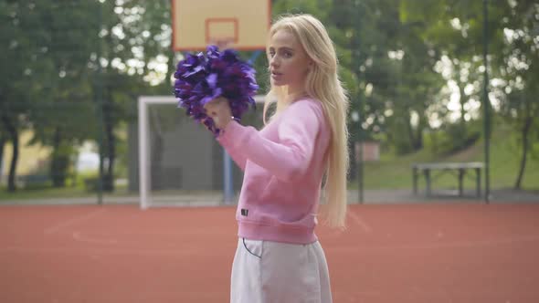 Cheerful Cheerleader Turning To Camera Shaking Pom-poms. Portrait of Beautiful Young Caucasian Woman