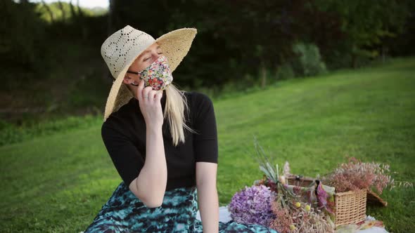 Cute woman with straw hat enjoys picnic in park taking off face mask, end of lockdown concept