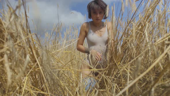 Graceful Woman with Short Hair Wearing Bodysuit Relaxing on the Wheat Field. Girl Enjoys Nature