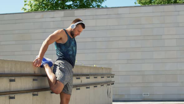 Young Man in Headphones Stretching Leg Outdoors