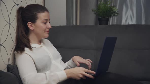 Young Girl Sitting on Sofa and Typing on Laptop Browsing Chatting in Internet