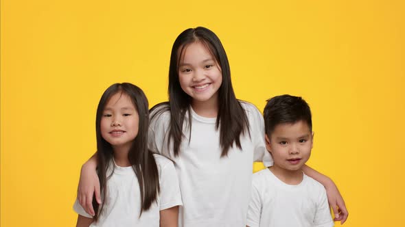 Happy Asian Girl Hugging Little Brother And Sister Yellow Background